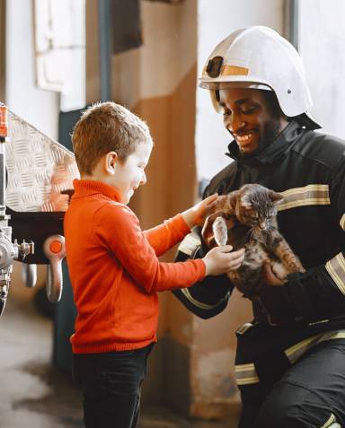 A firefighter with young boy smiling, as he holds a kitten. 