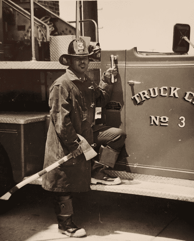 A firefighter in full uniform, including a helmet with a shield, smiling and standing next to a child