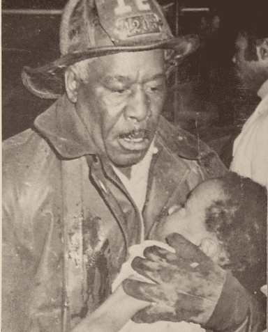 The firefighter looks off into the distance, holding the helmet securely with gloved hands