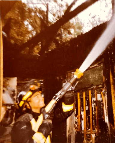 A firefighter wearing a helmet and full uniform examines equipment in a fire station